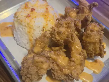 Camarones Bang Bang: camarones fritos y crujientes en salsa bang bang anaranjada, junto a un montoncito de arroz blanco, en una charola de acero.