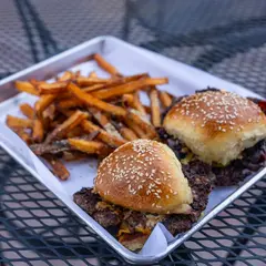 Dos hamburguesas smash y papas en sebo de res en una charola, en el patio.