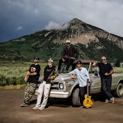 La banda Mountain Jam, con una camioneta vieja frente a una montaña.