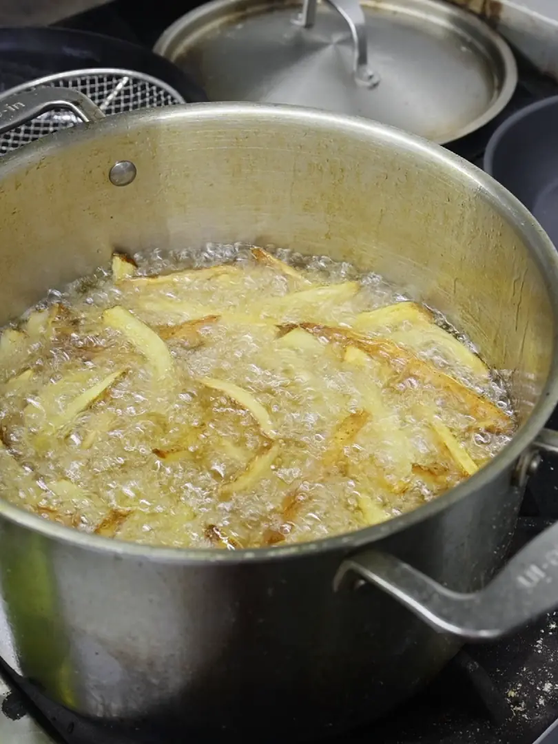 Papas burbujeando en una olla honda de acero con grasa caliente, en la estufa.