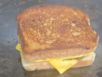 Un patty melt de Wagyu en la plancha, con el pan doradito y el queso derritiéndose por un lado.