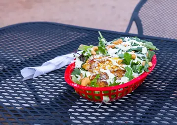 Una ensalada de pollo con hojas verdes, nuez de la India y un aderezo cremoso en una canasta roja, sobre una mesa de malla del patio.